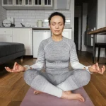 یوگا زن نشسته با لباس اسپرت خاکستری در وسط خانه
